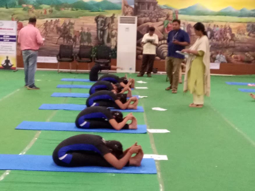 Advaitha Yoga students performing synchronized Paschimottanasana (seated forward bend) during yogasana championship competition in Hyderabad with judges inspecting form