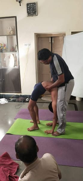 Advaitha Yoga coach guiding a young student into Chakrasana (Wheel pose drop-back) with hands-on alignment support