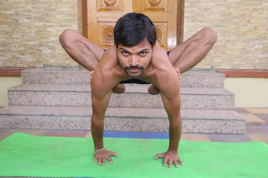 Yogi holding Bhujapidasana (shoulder-pressing arm balance) with legs crossed behind arms during advanced asana practice