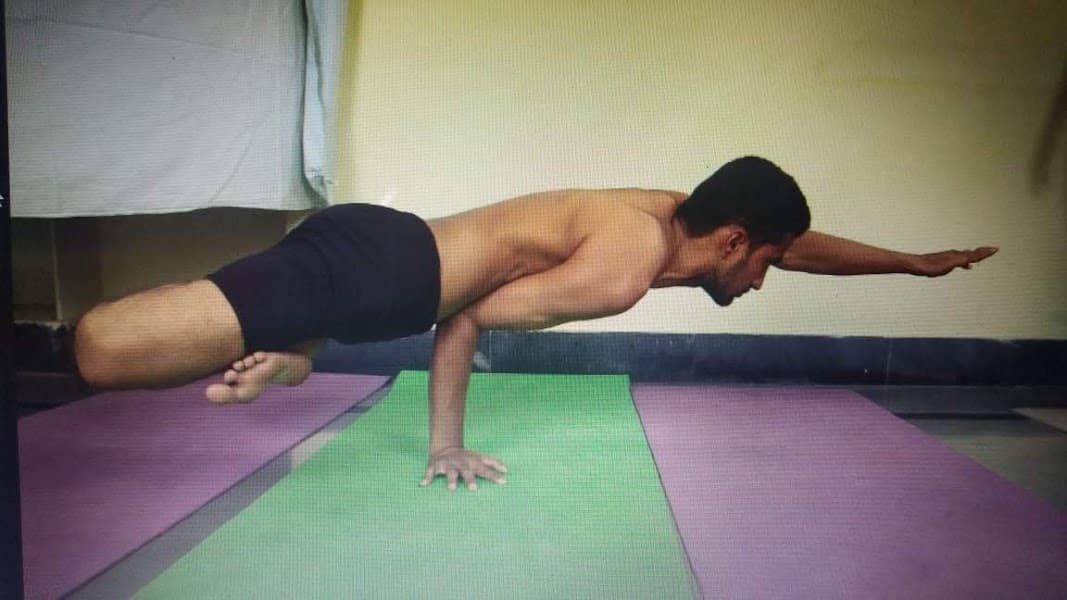 Advanced practitioner performing Eka Hasta Padma Mayurasana (one-handed Peacock Pose in lotus) demonstrating balance and core strength