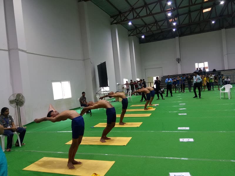 Junior competitors in blue shorts holding synchronized Hasta Uttanasana (standing backward bend) on yellow mats at state yoga championship
