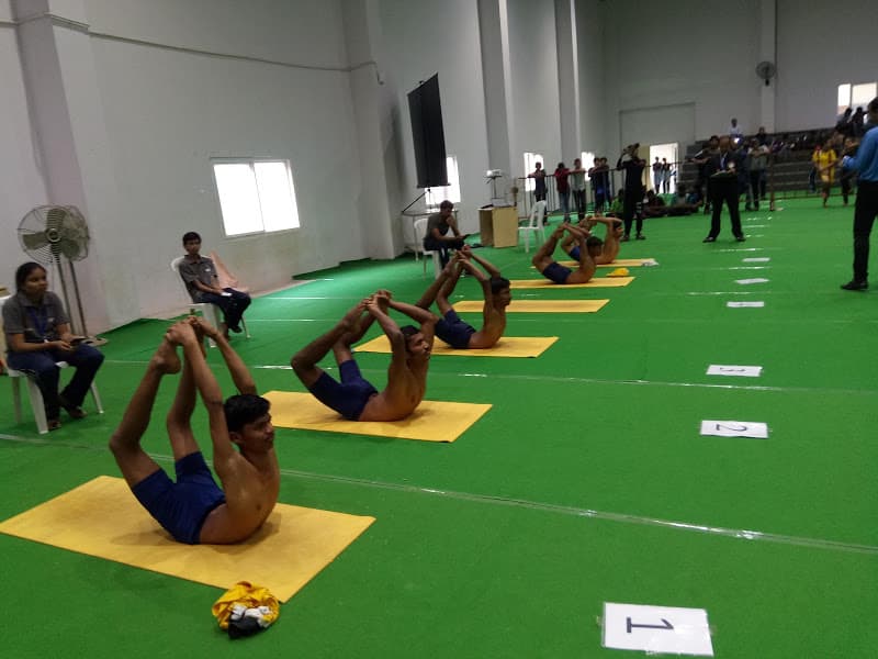 State championship competitors executing Padangustha Dhanurasana (full big-toe grip Bow Pose) in arena before referee panel