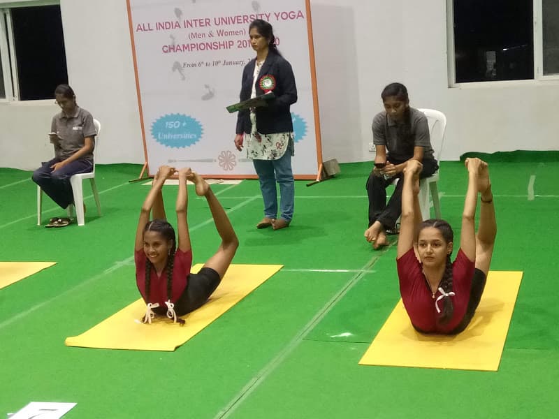 Two female students performing synchronized Padangustha Dhanurasana (full Bow Pose) at All India Inter University Yoga Championship